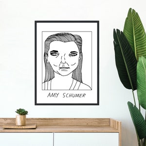May include: Black and white line drawing of Amy Schumer in a portrait style. The image is framed in a black frame and the text "AMY SCHUMER" is below the drawing.