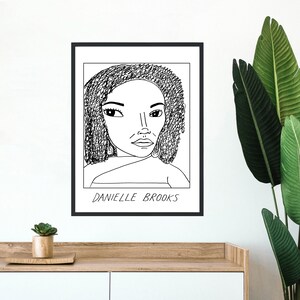May include: Black and white line drawing of a woman with curly hair. The drawing is framed in a black frame and the text "Danielle Brooks" is below the drawing.