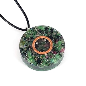 Könnte beinhalten: Ein runder grüner und schwarzer Kristall-Anhänger mit einem Kupferring in der Mitte, der an einer schwarzen Schnur hängt.