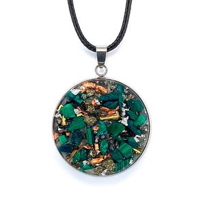 Könnte beinhalten: Eine runde Anhänger Halskette mit silberfarbener Lünette und schwarzem Band. Der Anhänger ist mit grünen Malachitsteinen, Kupfer und Silberflocken gefüllt. Die Halskette wird vor weißem Hintergrund präsentiert.