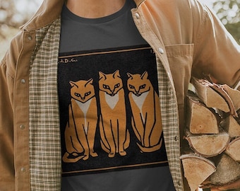 May include: Dark gray t-shirt featuring a graphic of three stylized orange cats with white accents, set against a black background with the text "A.D.C." The cats are in a row, with a simple, geometric design. The shirt is a casual wear item.