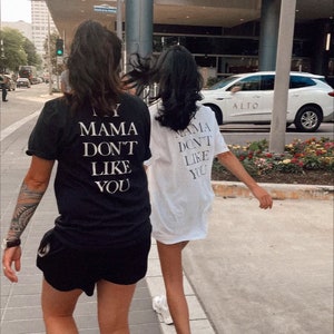May include: Two people wearing black and white t-shirts with the text "My Mama Don't Like You" printed on the back. The person in the black shirt is wearing black shorts.