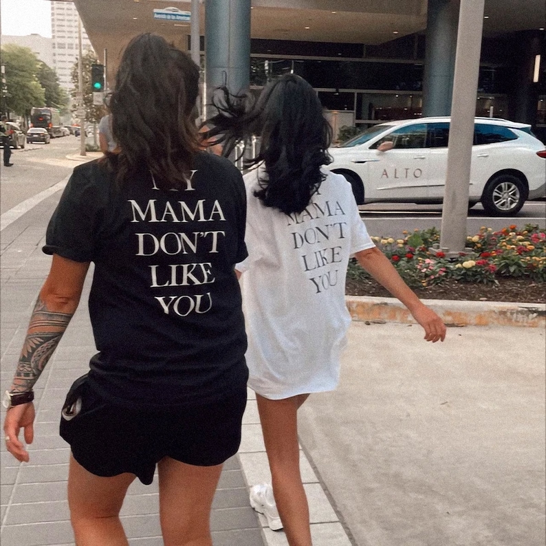 May include: Two people wearing black and white t-shirts with the text "My Mama Don't Like You" printed on the back. The person in the black shirt is wearing black shorts.
