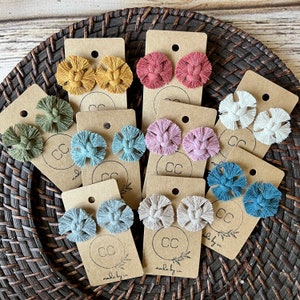 May include: Assortment of handmade macrame earrings displayed on cards with the text "CC made by cc". The earrings are in various colors, including blue, green, pink, and beige.