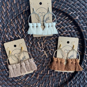 May include: Three pairs of handmade earrings with a macrame tassel design. The earrings are made with a gold or silver hoop and feature a white, brown, or rust colored tassel.