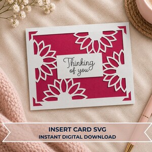 May include: A rectangular greeting card featuring a vibrant magenta background layered with a white die-cut frame and floral patterns. A central white rectangular label displays the black script text Thinking of you. The card design is clean and precise.