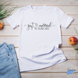 May include: White t-shirt with black text that reads "just married 40 years ago" with a heart symbol between the words "just" and "married".