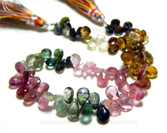 May include: A strand of multi-colored gemstone beads, including pink, green, blue, and brown, with a tassel at each end. The beads are faceted and have a pear shape.