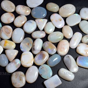 May include: A collection of over 40 white opal cabochons, displaying iridescent flashes of colour. The stones are of various shapes and sizes, including oval, round, and teardrop shapes. All stones are natural and have a smooth, polished finish.