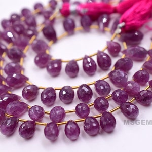 Könnte beinhalten: Eine Strähne aus violetten Edelsteinperlen in Tropfenform. Die Perlen sind auf goldenen Draht gefädelt und haben eine Größe von etwa 10 mm.