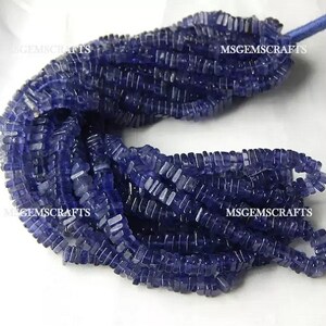 May include: A strand of blue gemstone beads, each bead is rectangular and faceted. The beads are strung on a clear thread and are approximately 10mm in length. The beads are arranged in a loose pile, with some of the beads overlapping. The beads are a deep blue color, with a slight purple hue. The beads are smooth and polished, with a slight sheen. The beads are perfect for making jewelry, such as necklaces, bracelets, and earrings.
