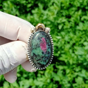 May include: A green and pink oval gemstone pendant with a silver and gold setting. The pendant is set in a silver bezel with a beaded edge and a gold bail.
