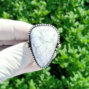 Puede incluir: Un anillo de plata con una piedra blanca y gris en forma de lágrima y detalles dorados.