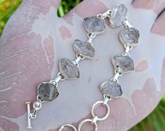 May include: A silver bracelet with a toggle clasp features a chain with clear, faceted, quartz crystal stones.