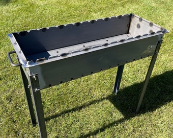 May include: A metal barbecue grill with a rectangular cooking surface and four legs. The grill is sitting on a green lawn.