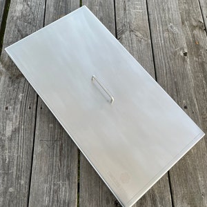 May include: A stainless steel fire pit cover with a handle. The cover has the words "Stainless Steel" printed on it.