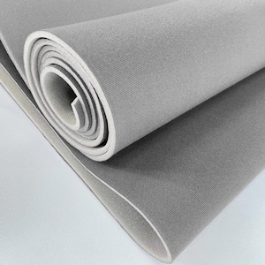 Puede incluir: Una esterilla de espuma gris enrollada con un borde blanco. La esterilla está hecha de un material suave y texturizado. El rollo revela el interior blanco y el exterior gris. La esterilla está desenrollada sobre una superficie blanca.