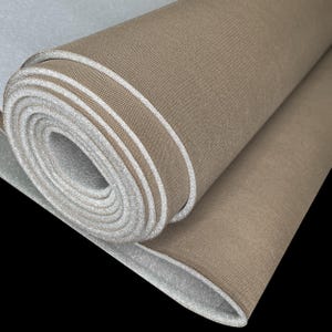 May include: Rolled-up tan fabric with white edges, possibly a mat or padding. The fabric has a textured surface and is partially unrolled, revealing the white interior. The background is black.