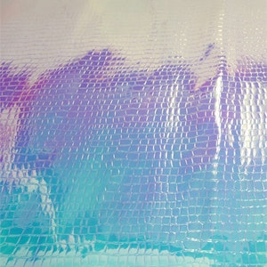 Op de afbeelding: Iridescent kunstleer met een textuur die op krokodillenleer lijkt. De kleur verschuift van lichtblauw naar paars, wat een glinsterend effect cre&euml;ert. Het oppervlak is reflecterend, waardoor het een glanzende uitstraling heeft. Geschikt voor diverse knutselprojecten.
