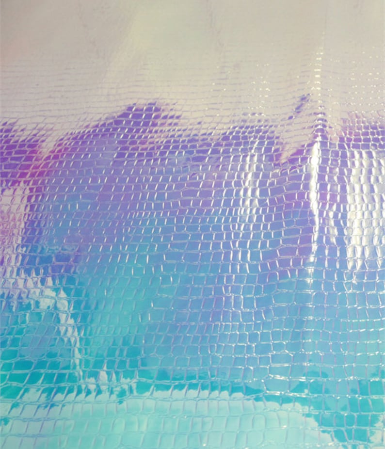 Op de afbeelding: Iridescent kunstleer met een textuur die op krokodillenleer lijkt. De kleur verschuift van lichtblauw naar paars, wat een glinsterend effect cre&euml;ert. Het oppervlak is reflecterend, waardoor het een glanzende uitstraling heeft. Geschikt voor diverse knutselprojecten.
