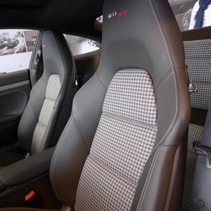 May include: Two black leather car seats with a grey and white houndstooth pattern. The seat on the right has the text "911 SO" embroidered in red on the headrest.