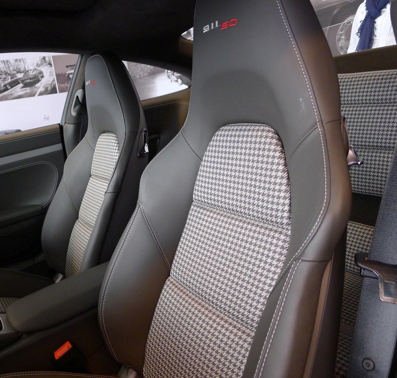 May include: Two black leather car seats with a grey and white houndstooth pattern. The seat on the right has the text "911 SO" embroidered in red on the headrest.