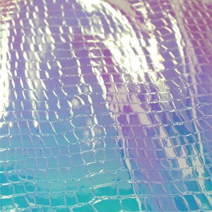 Op de afbeelding: Close-up van iriserend, getextureerd materiaal met een krokodil- of reptielschubbenpatroon. De kleurovergang gaat van blauw naar paars, met reflecterende highlights. Het materiaal lijkt flexibel en mogelijk gebruikt in mode of ambachten.