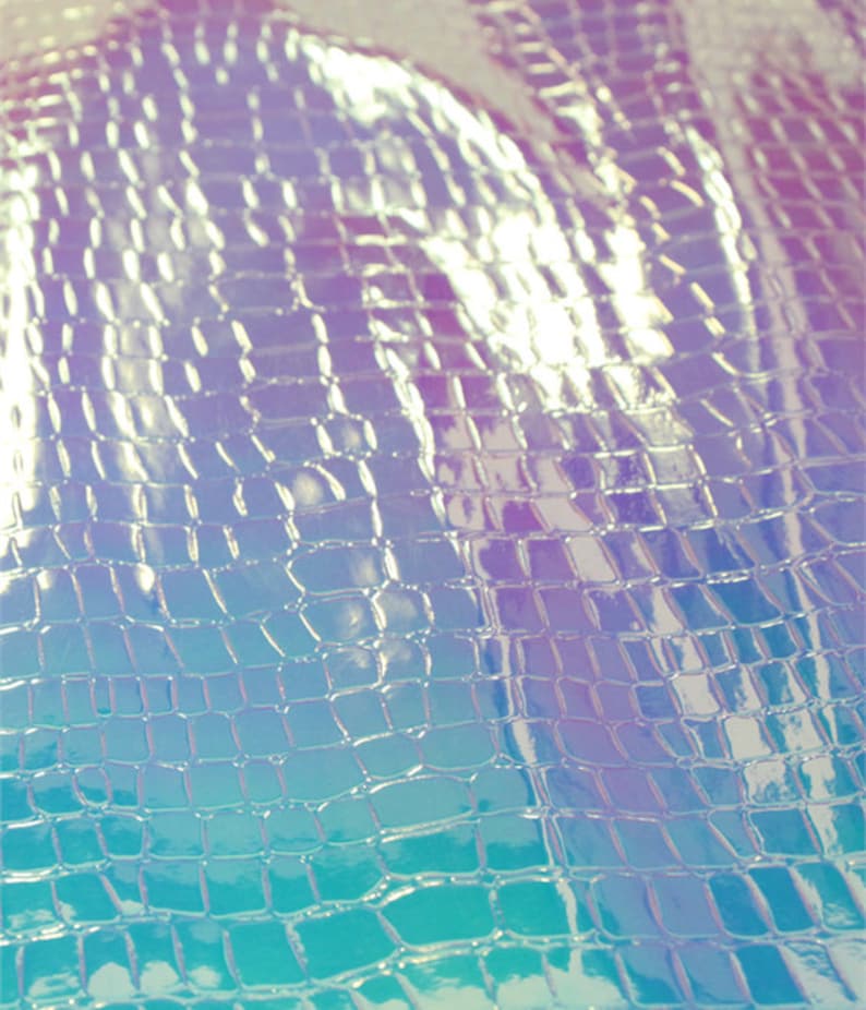Op de afbeelding: Close-up van iriserend, getextureerd materiaal met een krokodil- of reptielschubbenpatroon. De kleurovergang gaat van blauw naar paars, met reflecterende highlights. Het materiaal lijkt flexibel en mogelijk gebruikt in mode of ambachten.