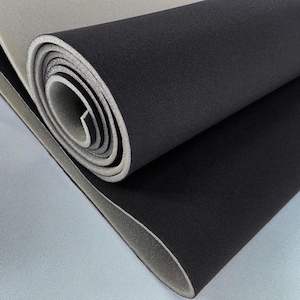 Puede incluir: Material de espuma negra enrollado con interior gris y respaldo gris claro. El material está parcialmente desenrollado, revelando las capas y la textura de la espuma. La imagen es un primer plano, destacando la superficie lisa y la forma enrollada.