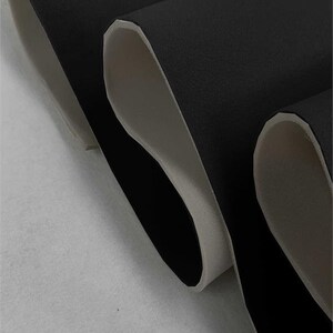 May include: Close-up of black fabric with a white backing. The fabric is folded in thirds, showing the white backing on the inside of each fold.