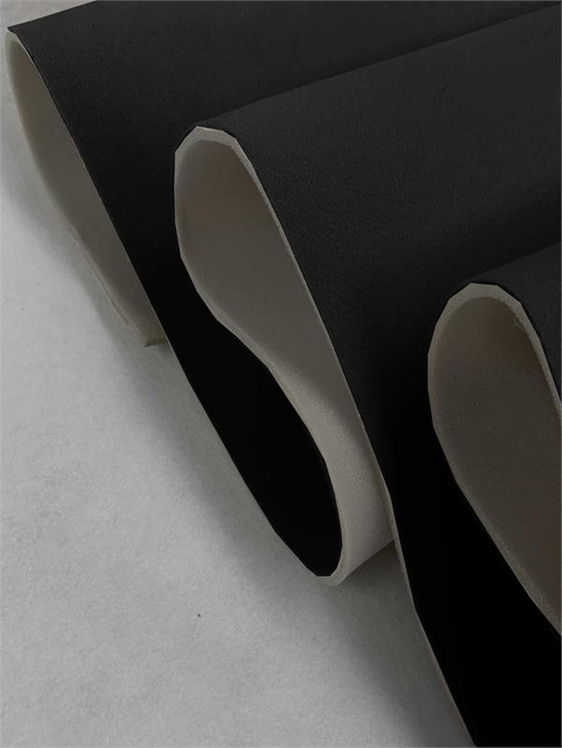 May include: Close-up of black fabric with a white backing. The fabric is folded in thirds, showing the white backing on the inside of each fold.