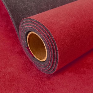 May include: A roll of dual-layered material featuring a vibrant red, textured, felt-like top surface and a contrasting black, fine-grained, glittery underside. The roll is tightly wound around a hollow, light brown cardboard cylindrical core.