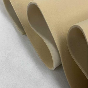 May include: Close-up of beige foam fabric rolled up. The fabric has a soft, velvety texture.
