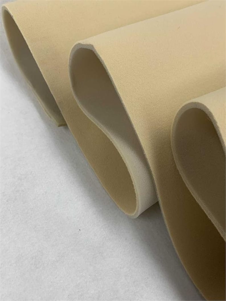 May include: Close-up of beige foam fabric rolled up. The fabric has a soft, velvety texture.