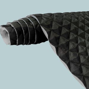 May include: A roll of black quilted fabric featuring a diamond-shaped stitched pattern. The material has a smooth, slightly reflective surface on the exterior and a light grey, felt-like backing visible on the inner layers of the roll.