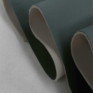 May include: Close-up of a dark teal fabric with a white backing. The fabric is folded over on itself, showing the white backing.