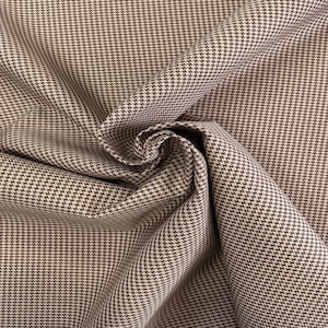 May include: Brown and white houndstooth fabric with a subtle sheen. The fabric is folded and draped, showcasing the pattern.