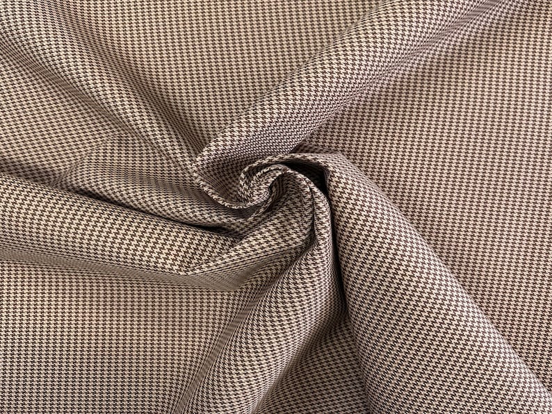 May include: Brown and white houndstooth fabric with a subtle sheen. The fabric is folded and draped, showcasing the pattern.