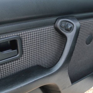 May include: Close-up of a black car door interior with a houndstooth pattern and a black door handle.