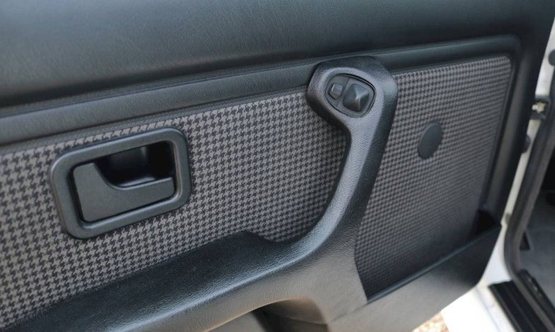 May include: Close-up of a black car door interior with a houndstooth pattern and a black door handle.