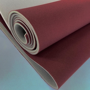 May include: A rolled sheet of dual-layered material featuring a deep burgundy red fabric top surface with a fine-grained texture and a smooth, light gray foam backing. The roll displays the layered cross-section of the flexible material.