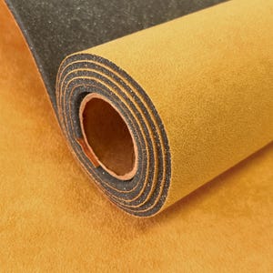 May include: A rolled sheet of material featuring a vibrant mustard yellow suede-like top surface and a contrasting black textured underside. The roll displays multiple layers of the dual-toned material, highlighting the distinct color difference between the sides.