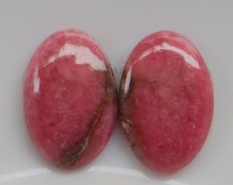 May include: Two oval-shaped pink and brown gemstone cabochons on a white background.