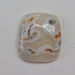 以下が含まれることがあります： 茶色と緑色のインクルージョンが入った白いアゲートのcabochon。石は長方形にカットされ、研磨仕上げが施されています。