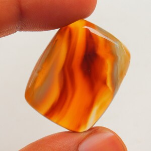 Op de afbeelding: Een gladde, gepolijste, oranje agaat cabochon met witte en bruine banden. De steen is rechthoekig van vorm en heeft een glanzende afwerking.