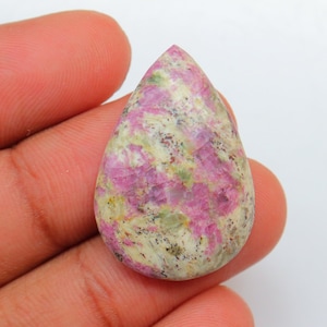May include: A teardrop-shaped cabochon gemstone with a pink and white marbled pattern. The stone has a rough, natural texture.