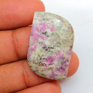 May include: A cabochon of pink and white gemstone with a mottled pattern. The stone is irregularly shaped and has a smooth, polished surface.