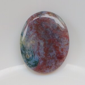 May include: A smooth, oval-shaped agate cabochon with a swirling pattern of red, blue, and white.