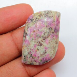 以下が含まれることがあります： ピンクと白のモザイク模様の、カボションカットされた宝石。石は不規則な形をしていて、滑らかで磨かれた表面をしています。