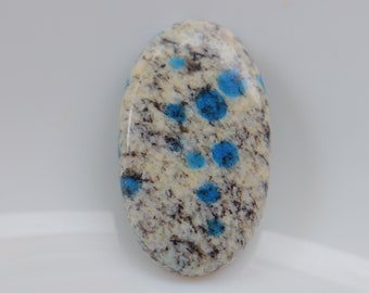May include: Oval shaped blue and white speckled stone cabochon. The stone has a white base with blue speckles throughout.